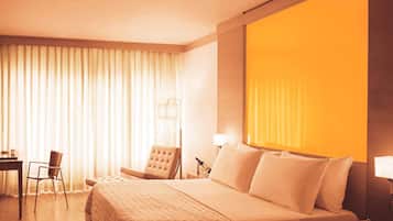 Hotelkamer met een groot bed, een bureau, een stoel en een nachtkastje met een lamp.