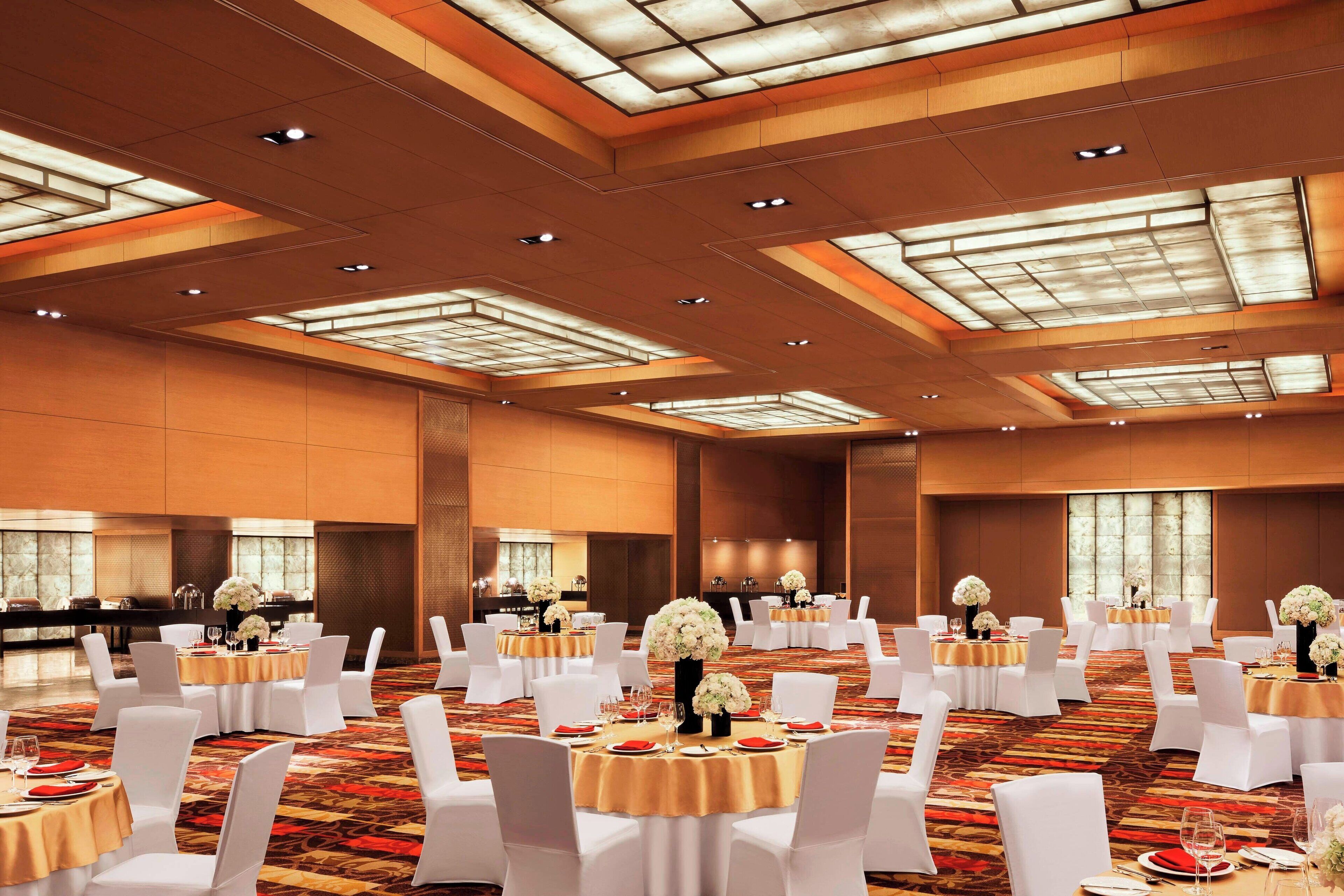Un amplio salón de banquetes con mesas redondas, sillas blancas y centros de mesa florales.