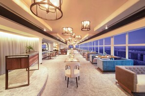 A spacious hotel lobby with a long reception desk, multiple seating areas, and large windows offering city views. - Le Meridien New Delhi (New Delhi)