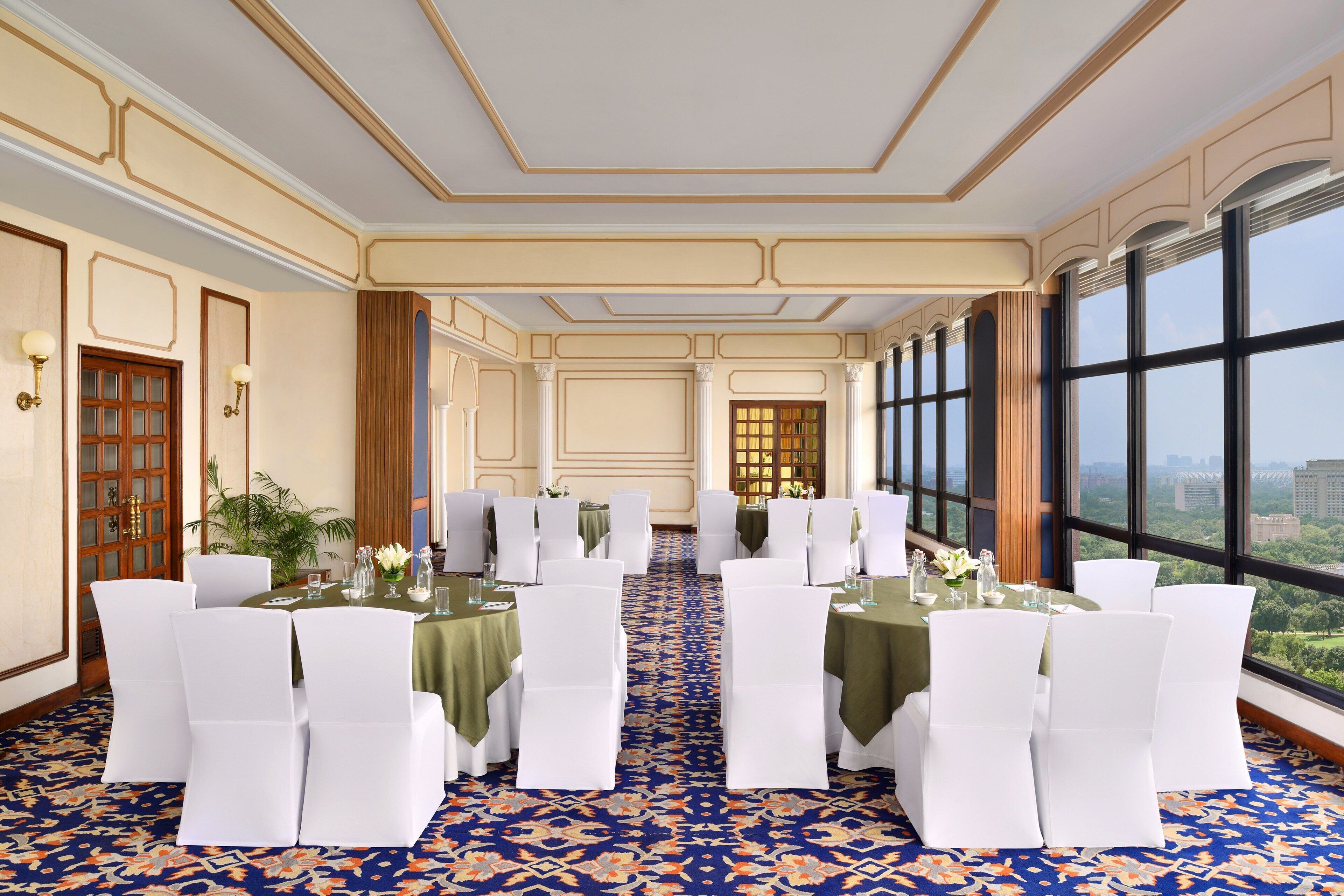 A banquet hall with tables set for a formal event, large windows offering a city view, and a patterned carpet.
