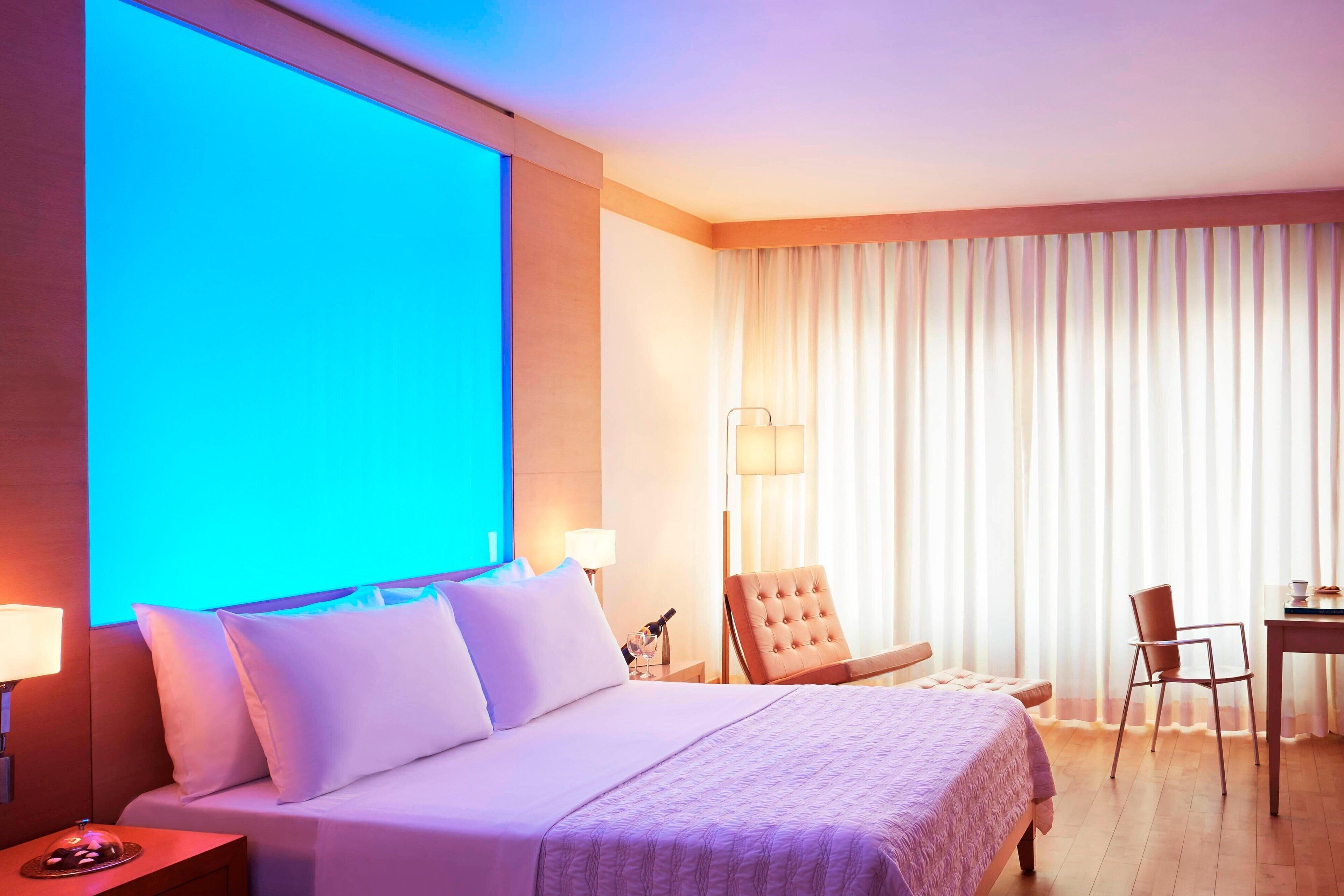A hotel room with a large bed, a desk, two chairs, a lamp, and a view of the outdoors.