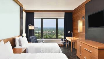 Hotelkamer met twee bedden, een bureau, een stoel en een groot raam met uitzicht op de stad.