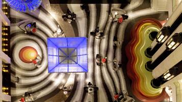 Vista cenital de un vestíbulo de hotel con una lámpara azul central, varias zonas de estar y una escalera de caracol.