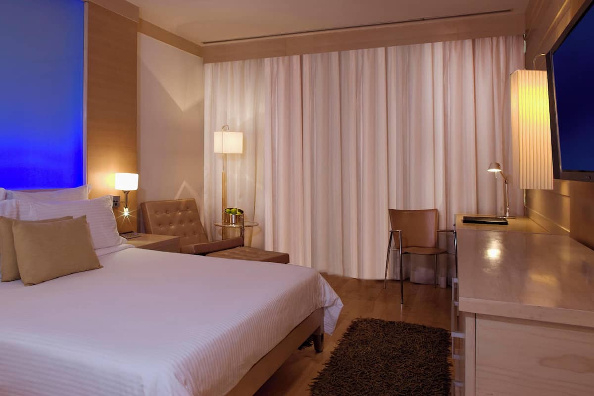 A hotel room with a large bed, a desk, a chair, and a TV.