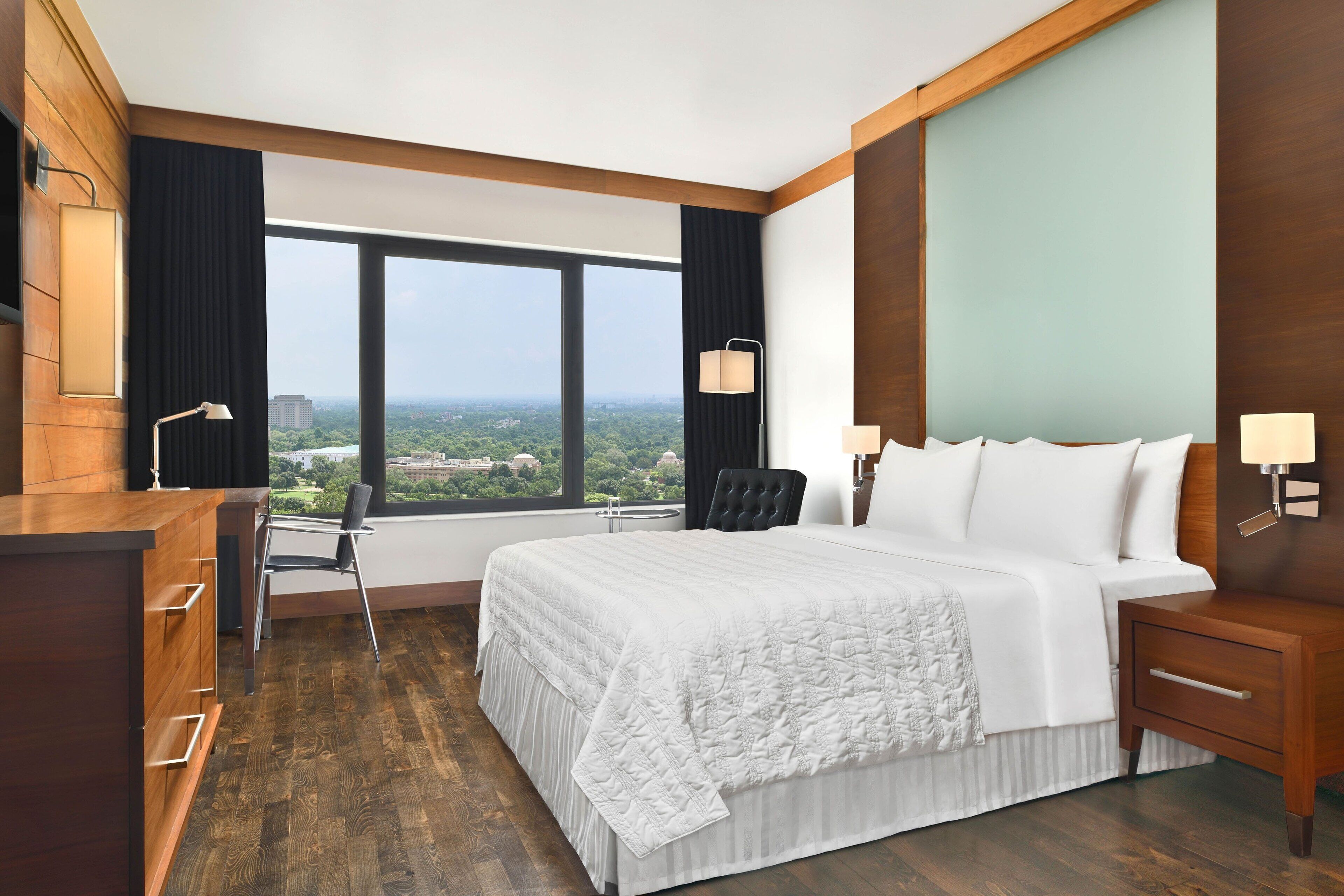 Een hotelkamer met een groot bed, een bureau, een stoel en uitzicht op de stad.