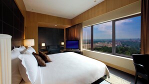 A hotel room with a large bed, a TV, a desk, and a view of the city. - Le Meridien New Delhi (New Delhi)