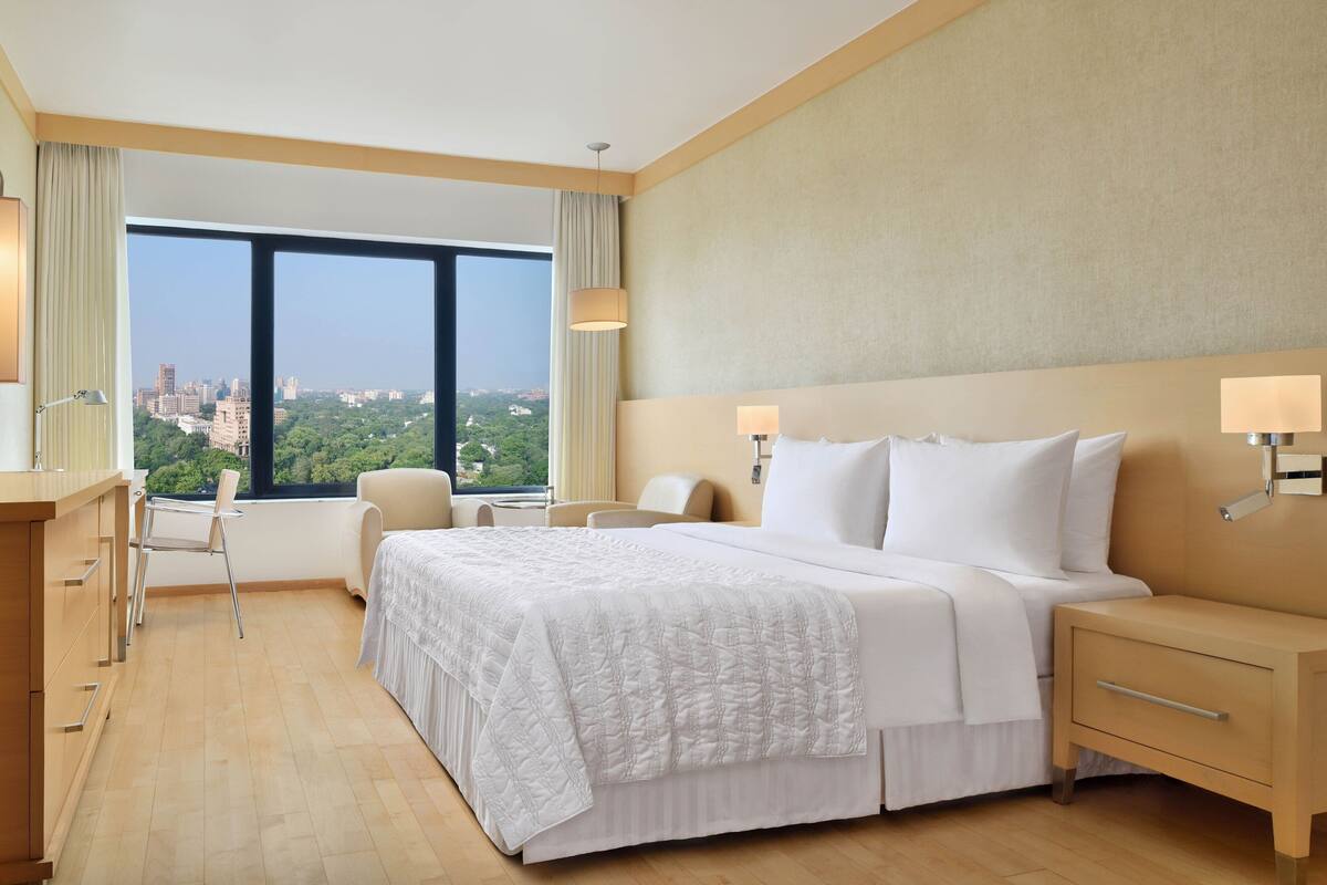 A hotel room with a large bed, a desk, a chair, and a view of the cityscape.
