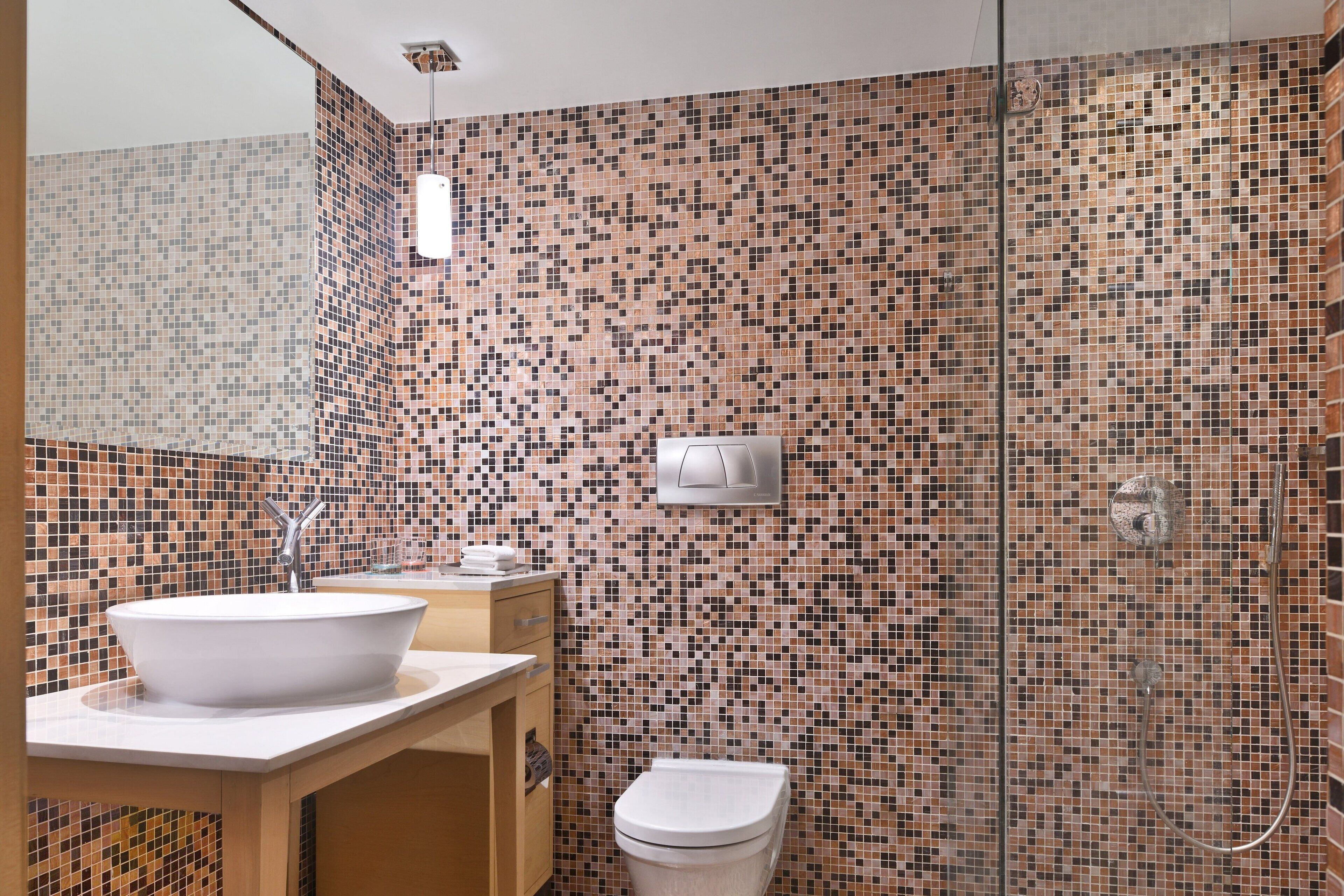 A bathroom with a mosaic tile wall, a white sink, and a toilet.