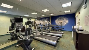 Ein Fitnessstudio mit Laufbändern, Kraftgeräten und einem Wandbild mit Löwenzahn.