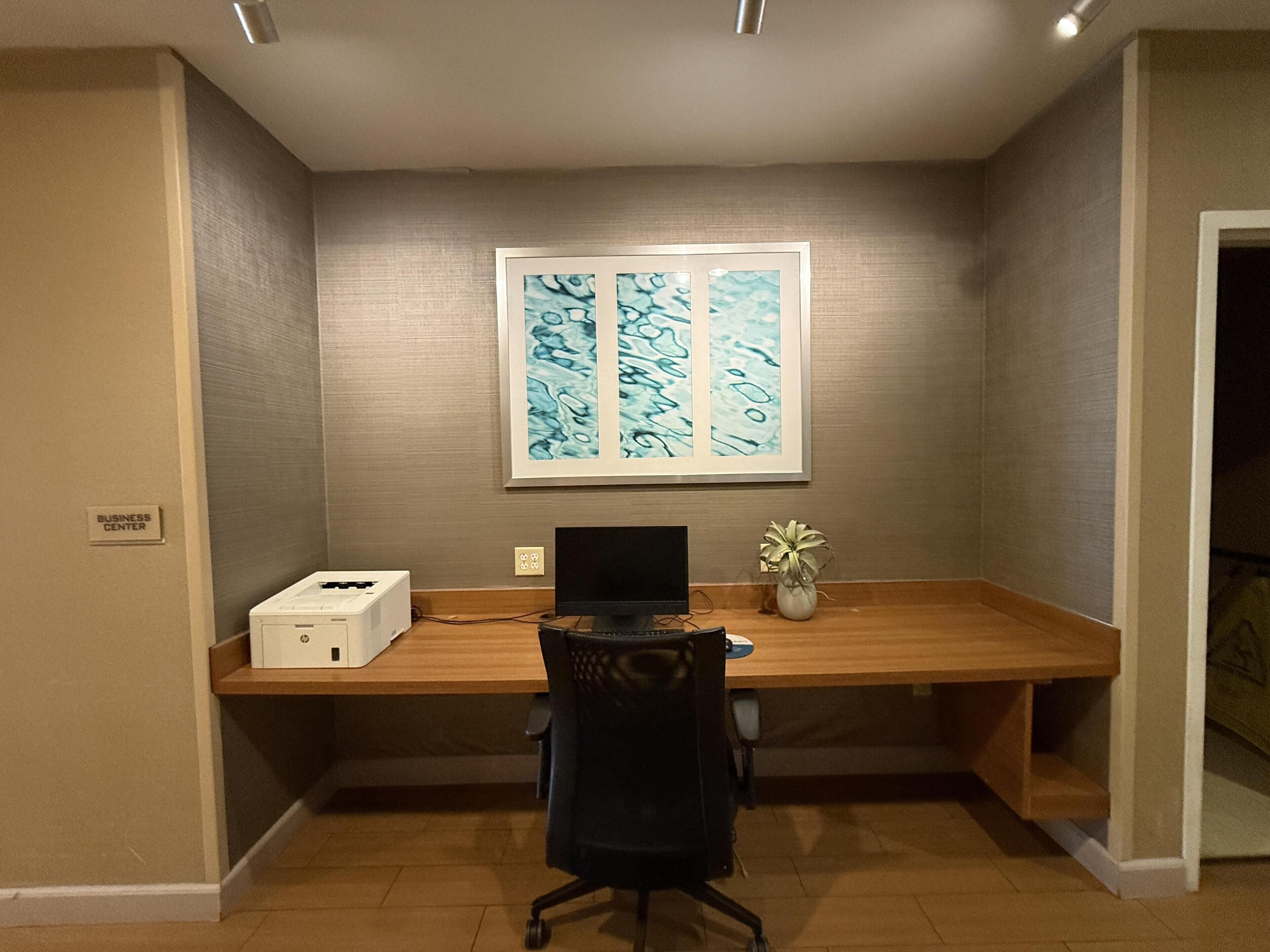 Un bureau à domicile équipé d’un bureau, d’un ordinateur portable, d’une imprimante et d’une œuvre d’art encadrée accrochée au mur.