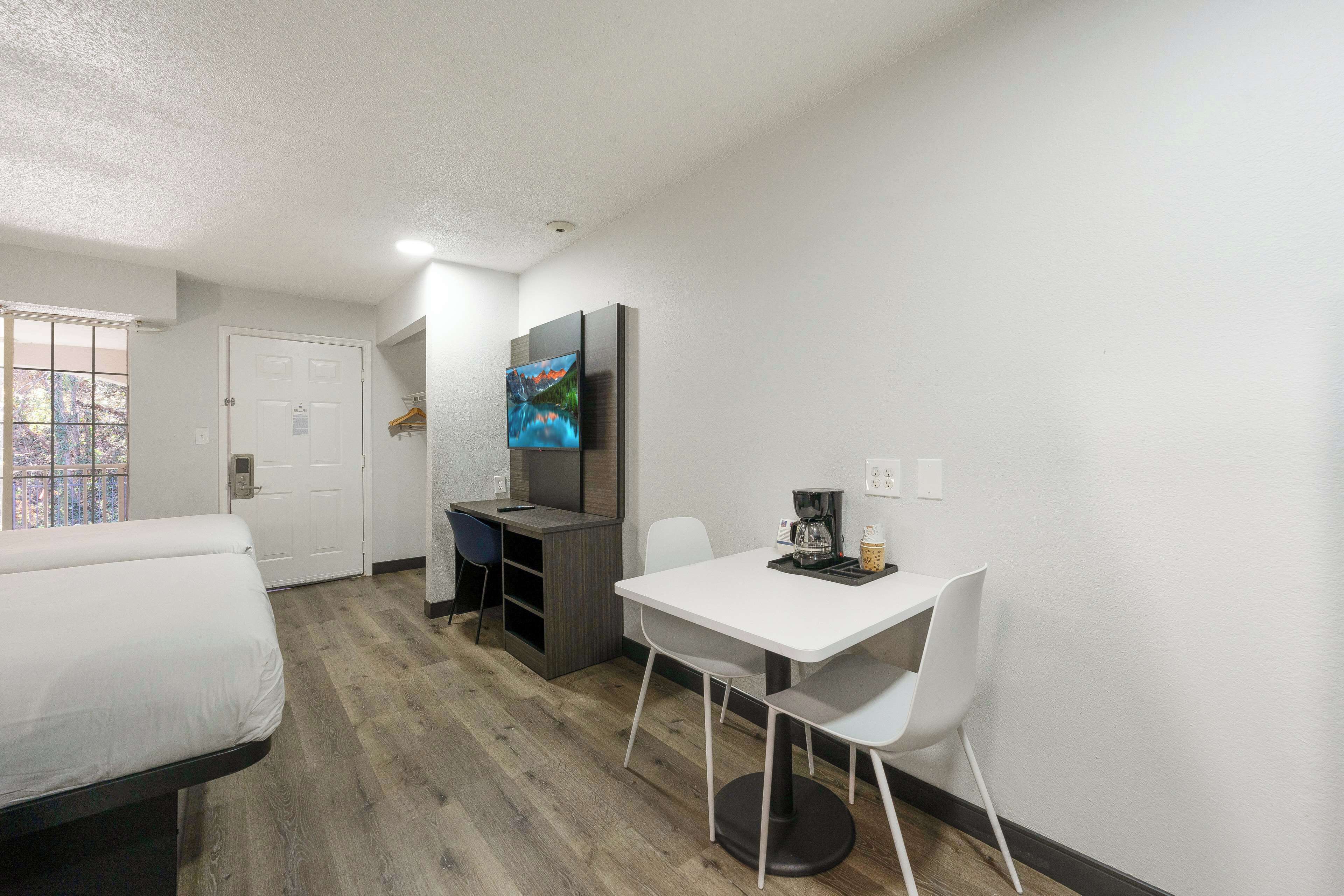 Una habitación de hotel con cama, escritorio, silla, televisor y cafetera.