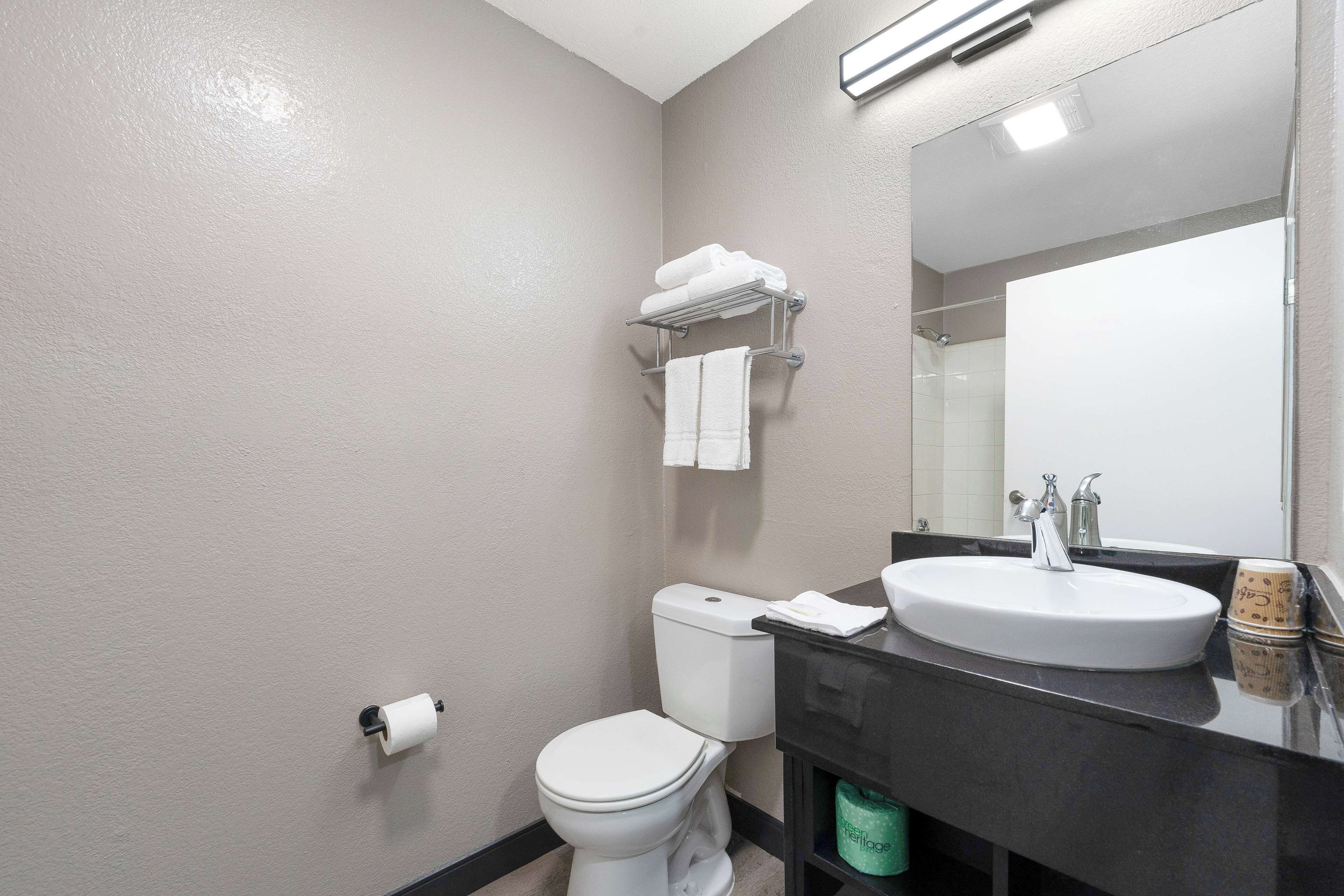 A bathroom with a white toilet, a sink with a mirror above it, and a towel rack with folded towels.