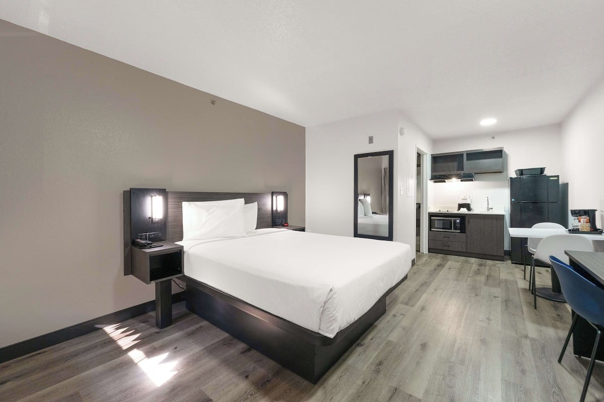 Ein modernes Hotelzimmer mit einem großen Bett, Nachttischen, einem Schreibtisch und einer Küchenzeile.