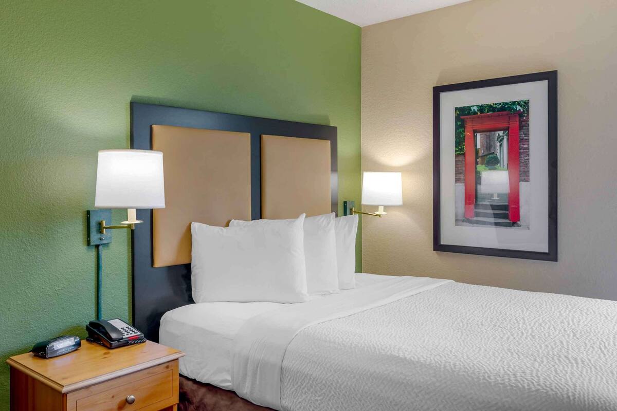 A hotel room with a bed, bedside lamps, a telephone, and a framed picture on the wall.