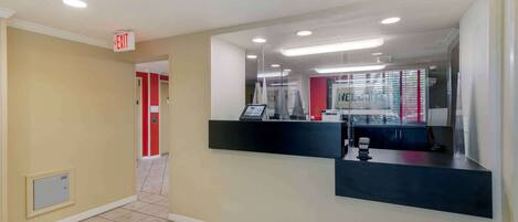 A hotel reception area with a modern design, including a reception desk, a red door, and a visible exit sign.