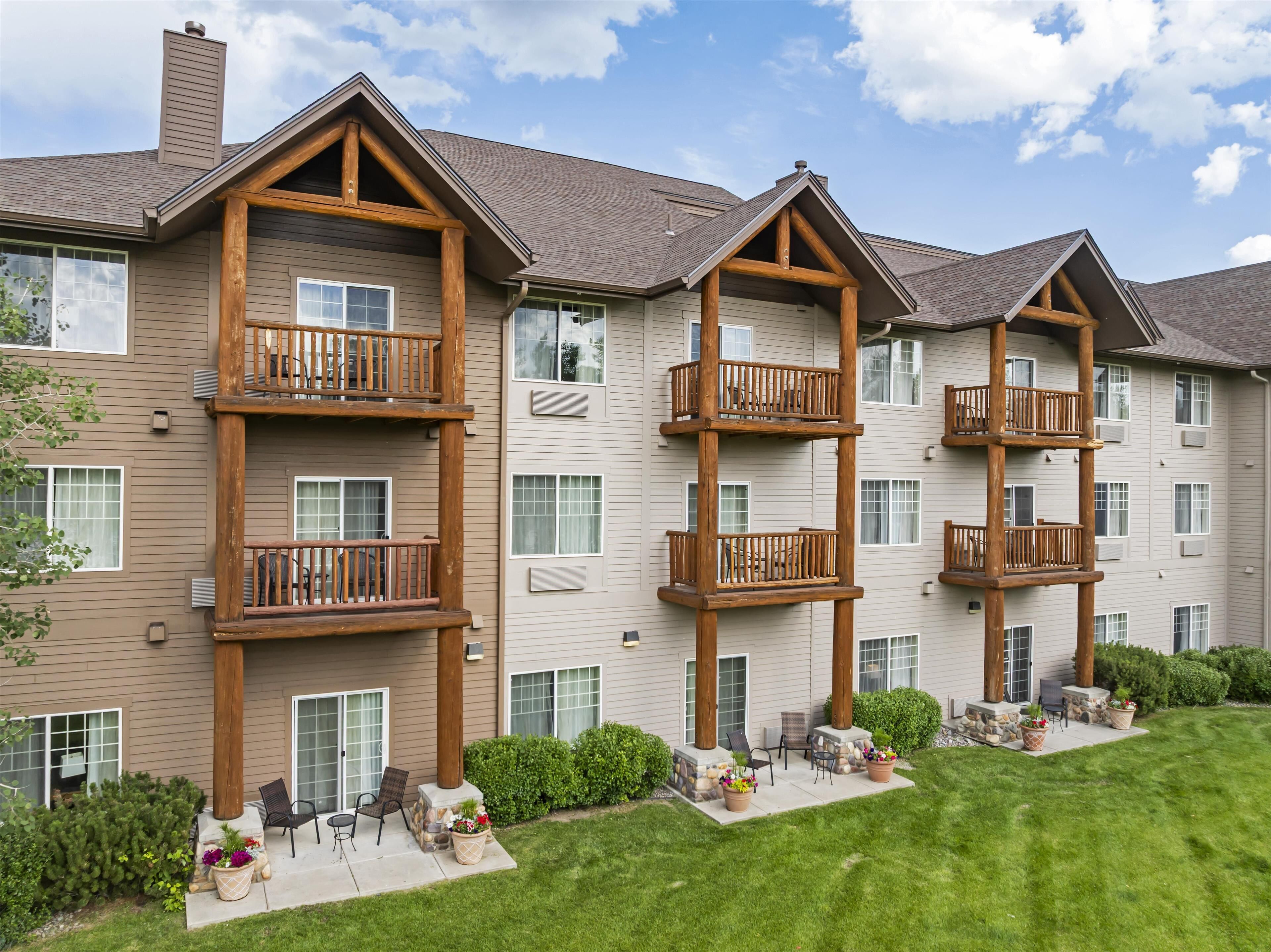 Un immeuble à plusieurs étages doté de balcons en bois, de fondations en pierre et d’une pelouse bien entretenue.
