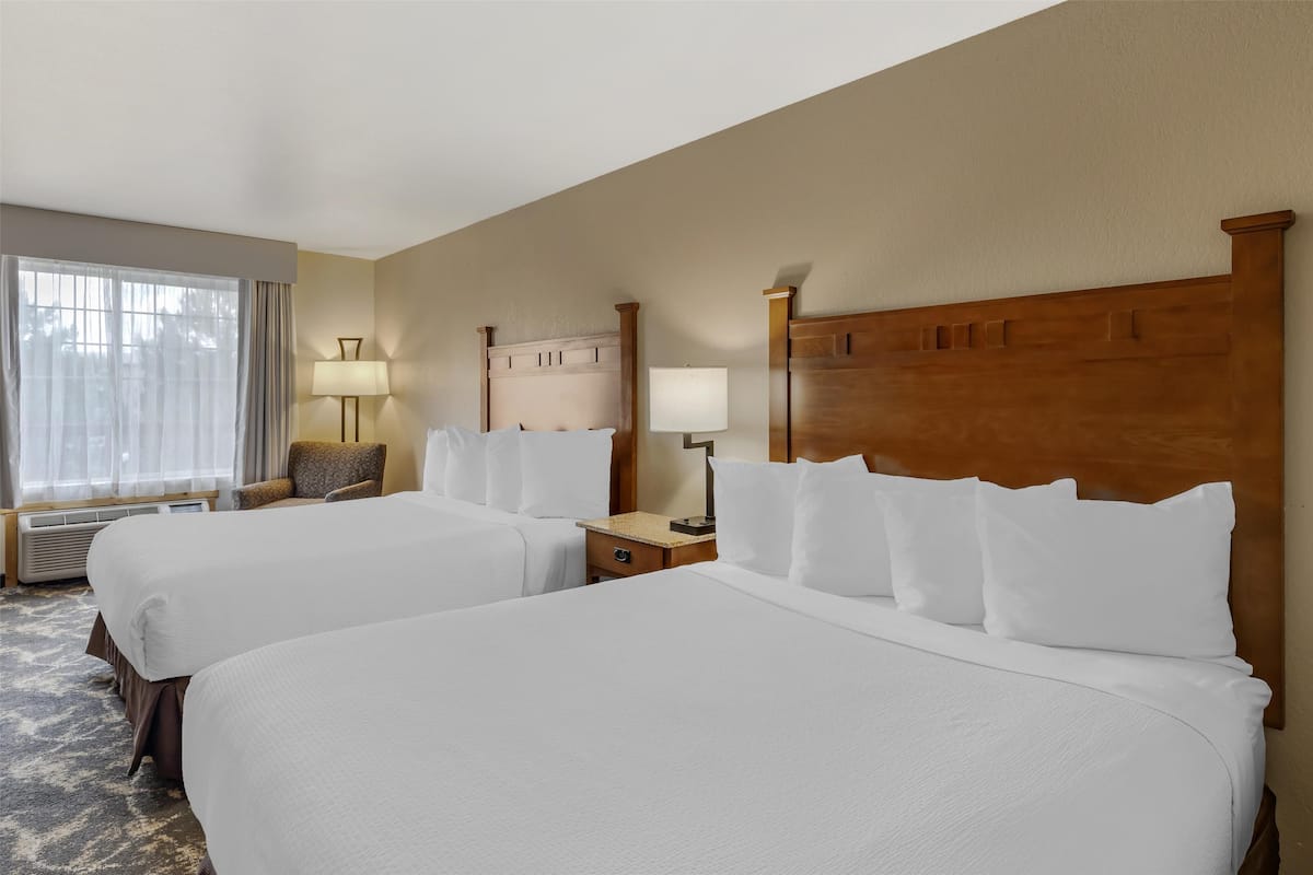 Ein Hotelzimmer mit zwei Betten, einem großen Fenster mit Vorhängen, einer Lampe und einem Nachttisch.
