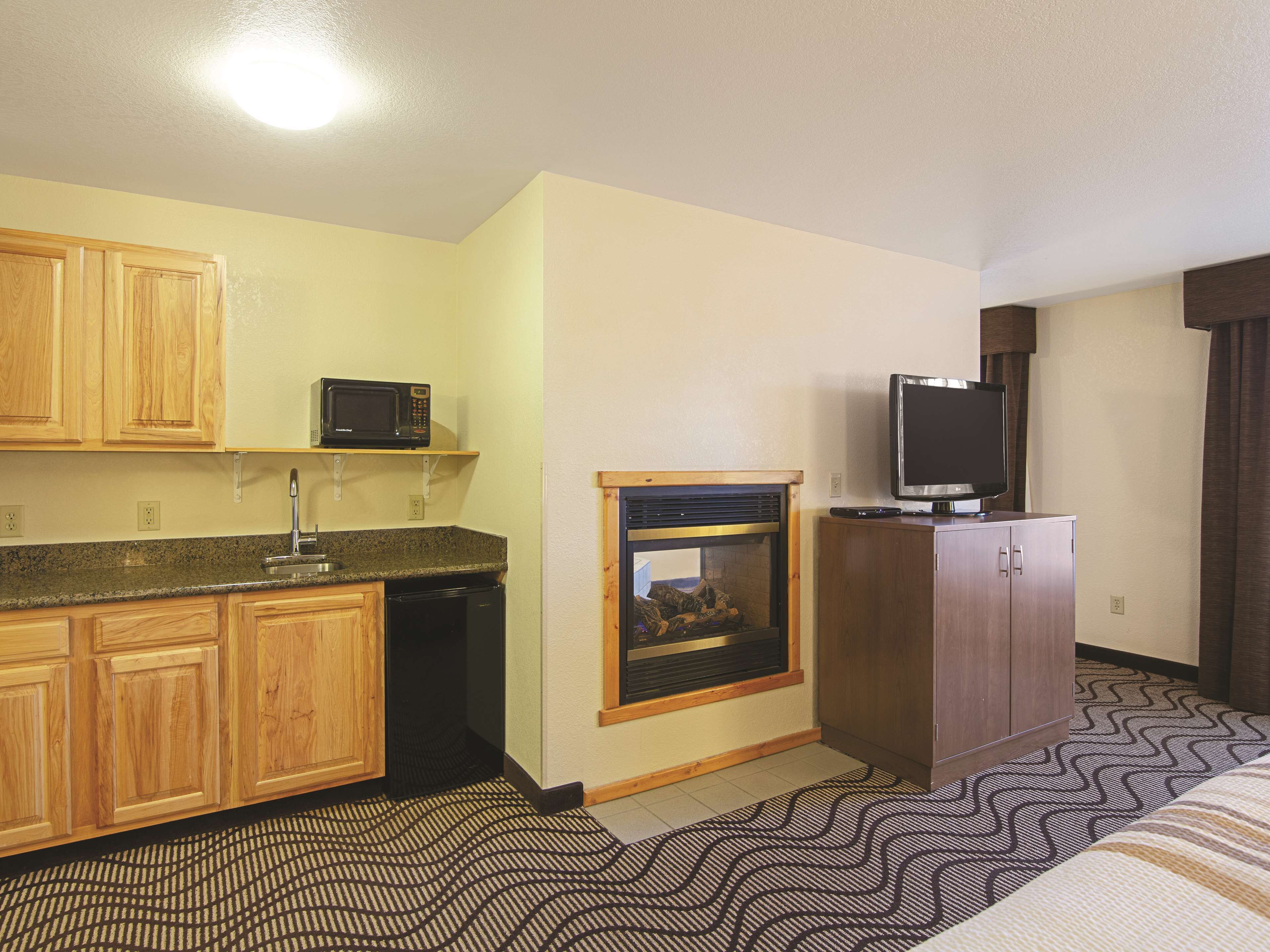 A compact hotel room with wooden cabinets, a microwave, a television, and a fireplace.