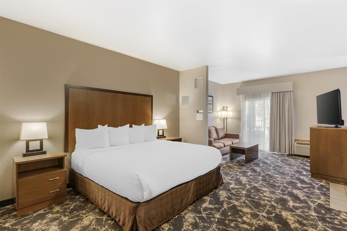 Ein Hotelzimmer mit einem großen Bett, einem Schreibtisch mit Fernseher, einem Sessel und einer Lampe.