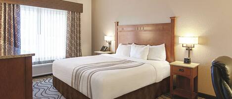 A hotel room with a large bed, two bedside tables with lamps, a desk, and a chair.