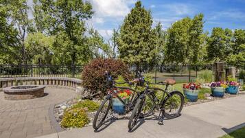Un espacio exterior empedrado con un pozo de fuego de piedra circular, una bicicleta y macetas con plantas.