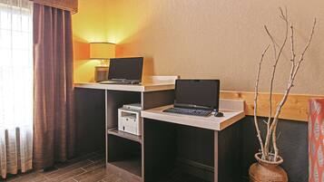 Een hotelkamer met twee bureaus, elk met een laptop en een lamp. Op het ene bureau staat een printer en op het andere een vaas met takken.