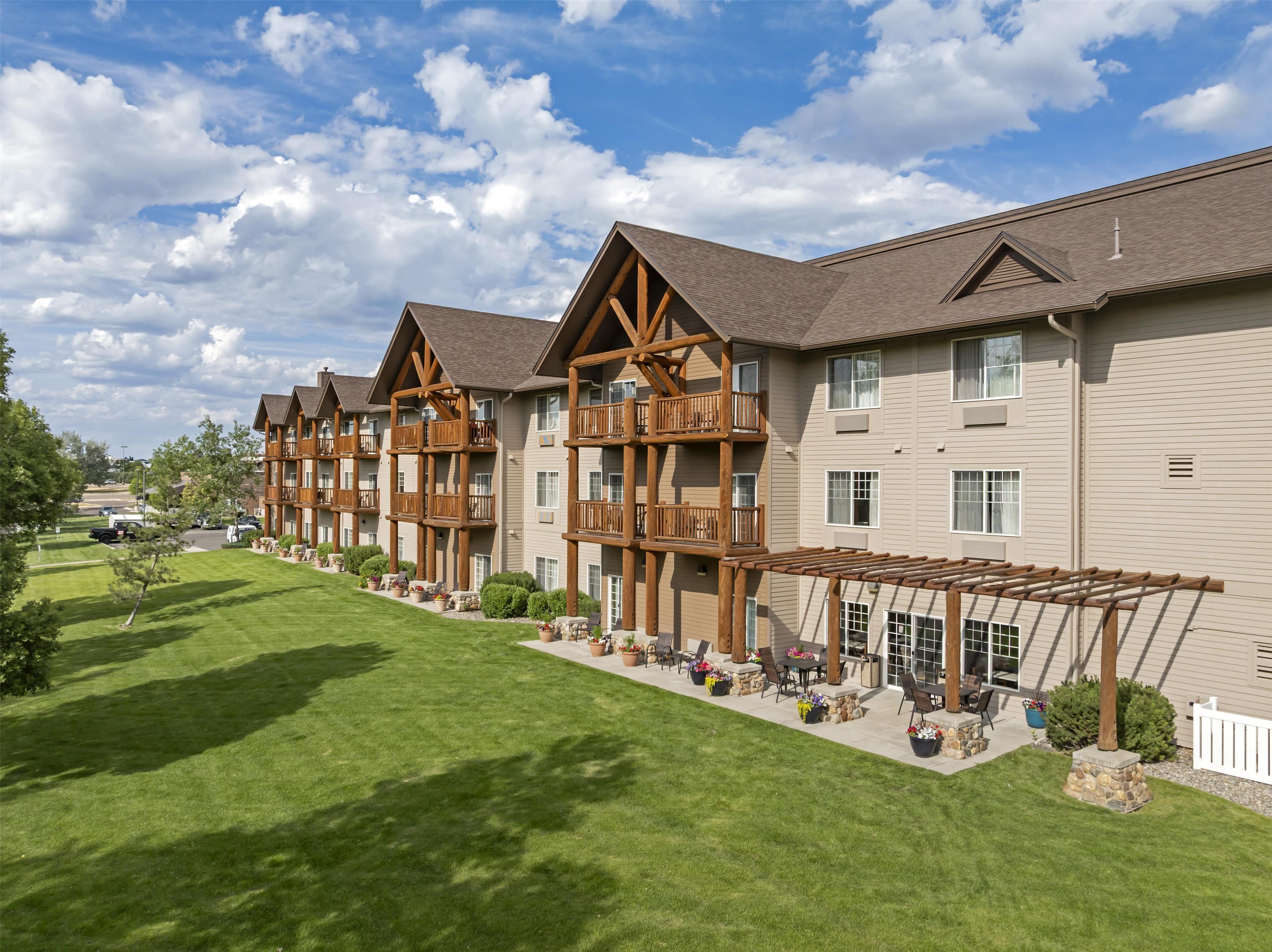 A row of multi-story buildings with balconies, a covered outdoor seating area, and a well-maintained lawn.