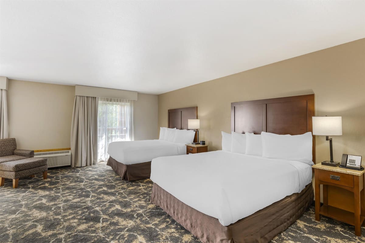 Ein Hotelzimmer mit zwei Betten, einem Sessel, einem Schreibtisch und einer Lampe.
