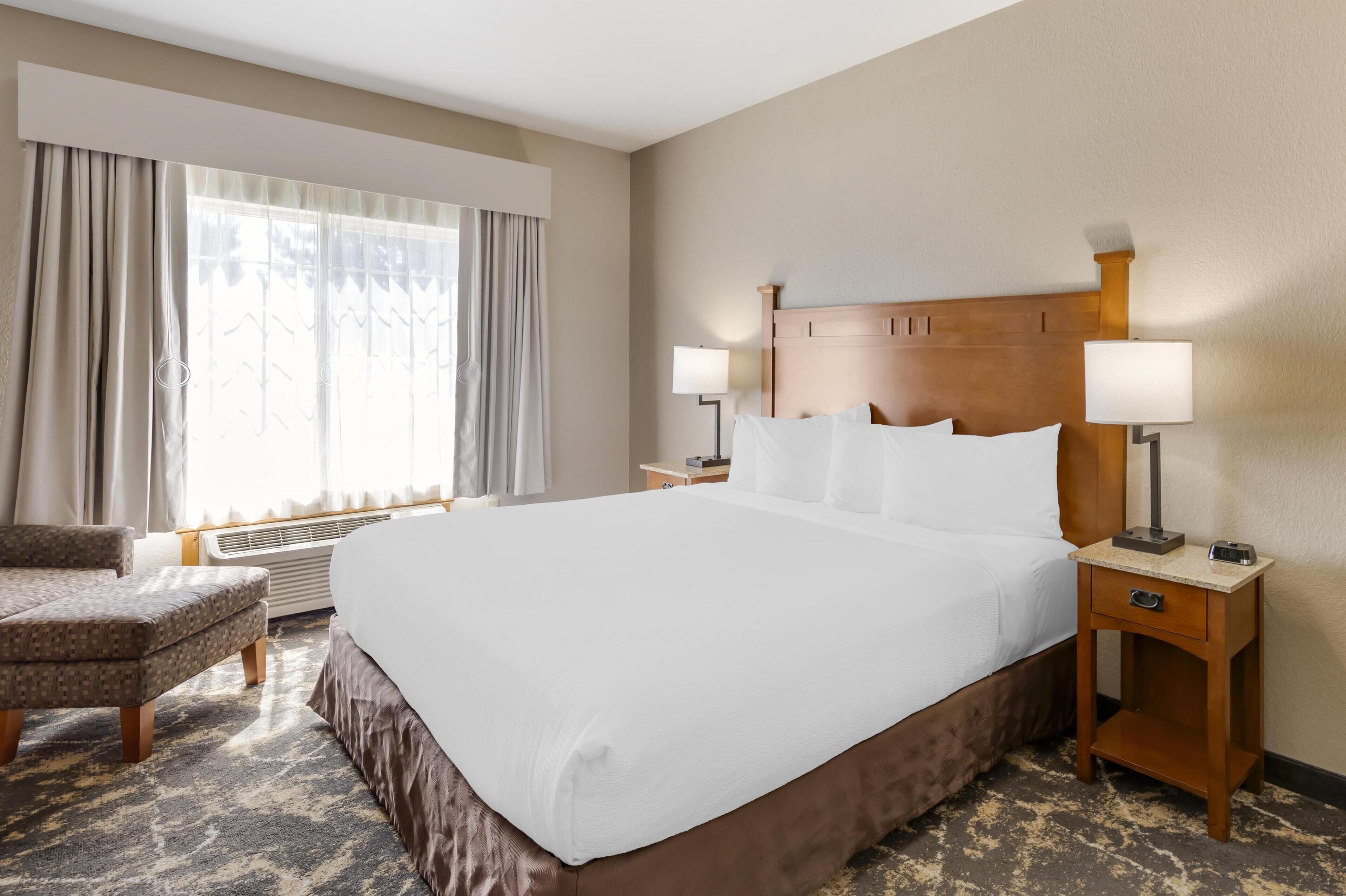 A hotel room with a large bed, two bedside tables with lamps, a chair, and a window with curtains.