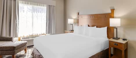 Habitación de hotel con una cama grande, dos mesitas de noche con lámparas, una silla y una ventana con cortinas.