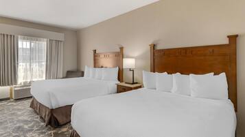A hotel room with two beds, a nightstand with a lamp, a window with curtains, and a carpeted floor.