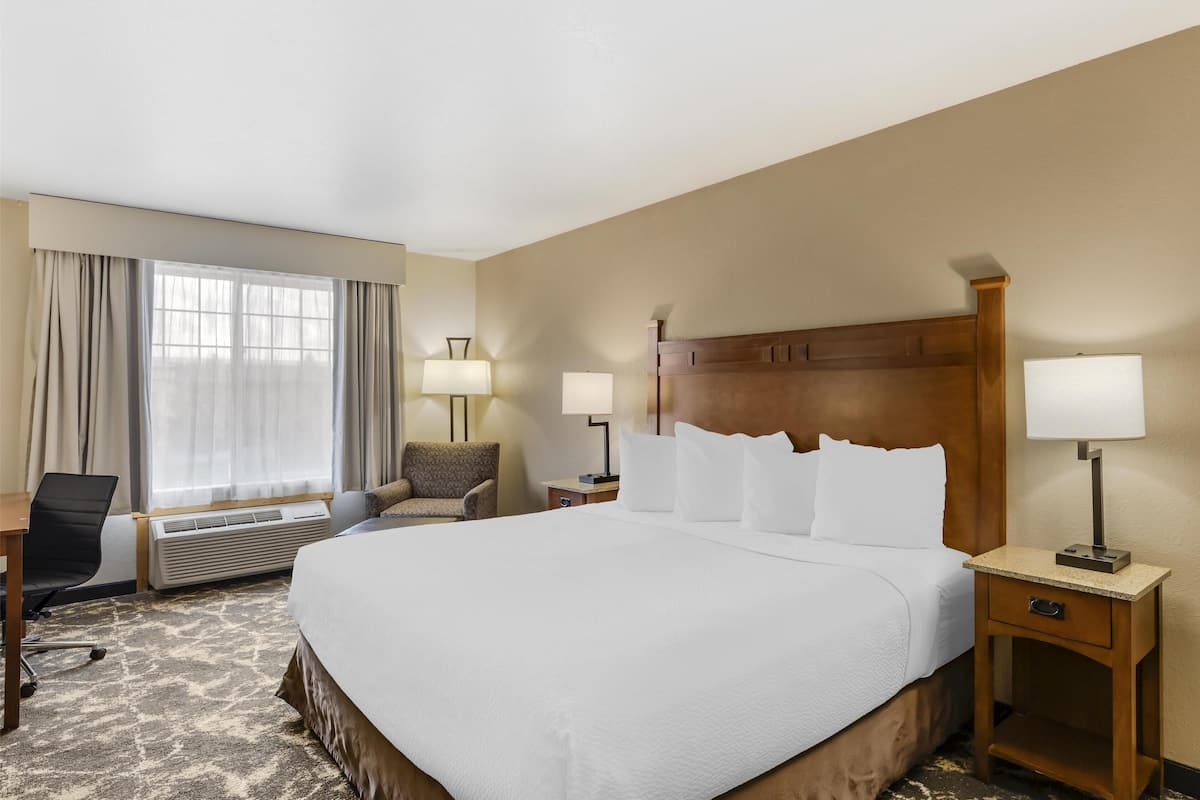 Ein Hotelzimmer mit einem großen Bett, zwei Nachttischen mit Lampen, einem Sessel, einem Schreibtisch und einer Klimaanlage.