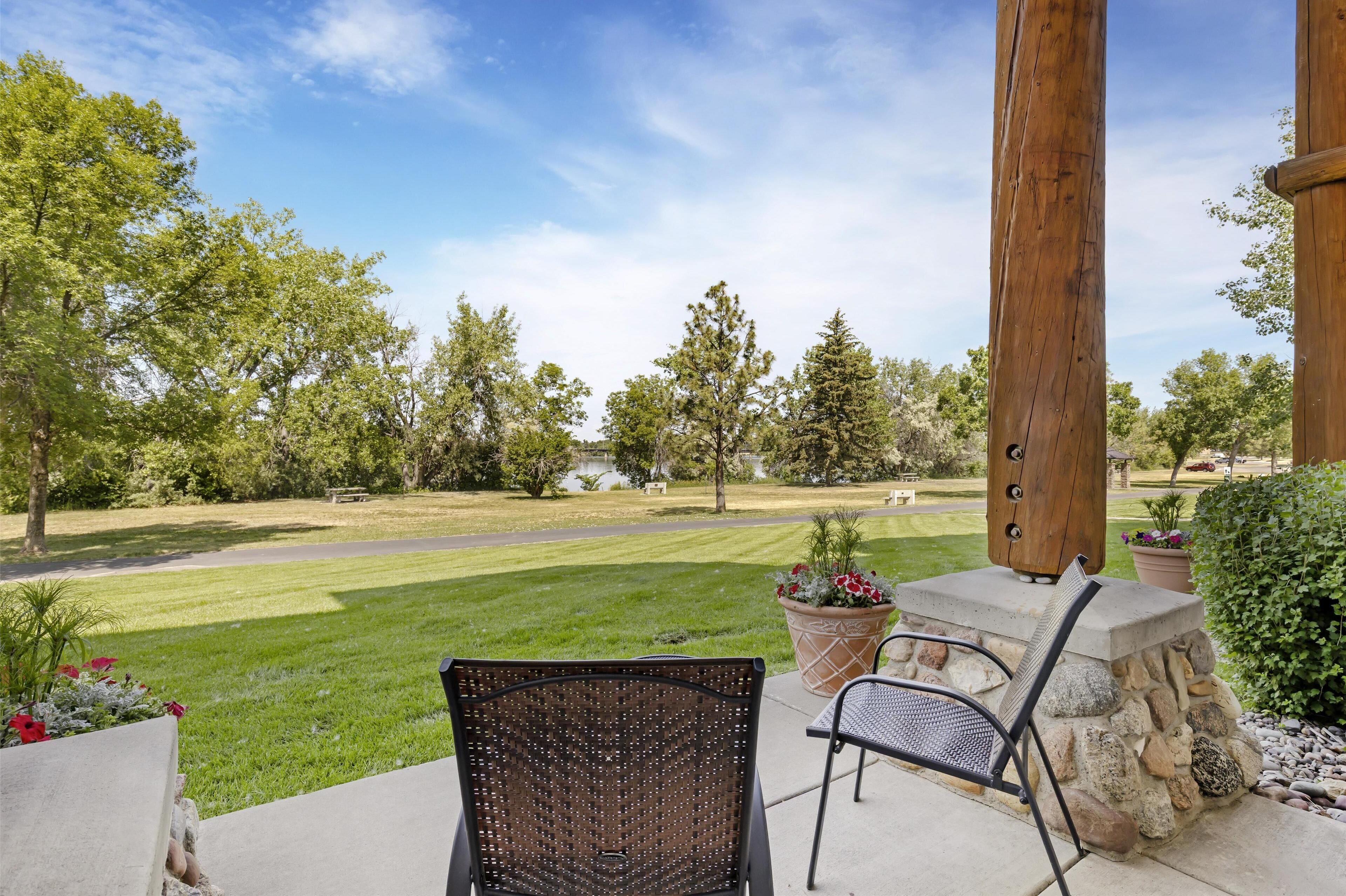 A patio area with outdoor furniture, a stone wall, and a view of a well-maintained lawn and trees.