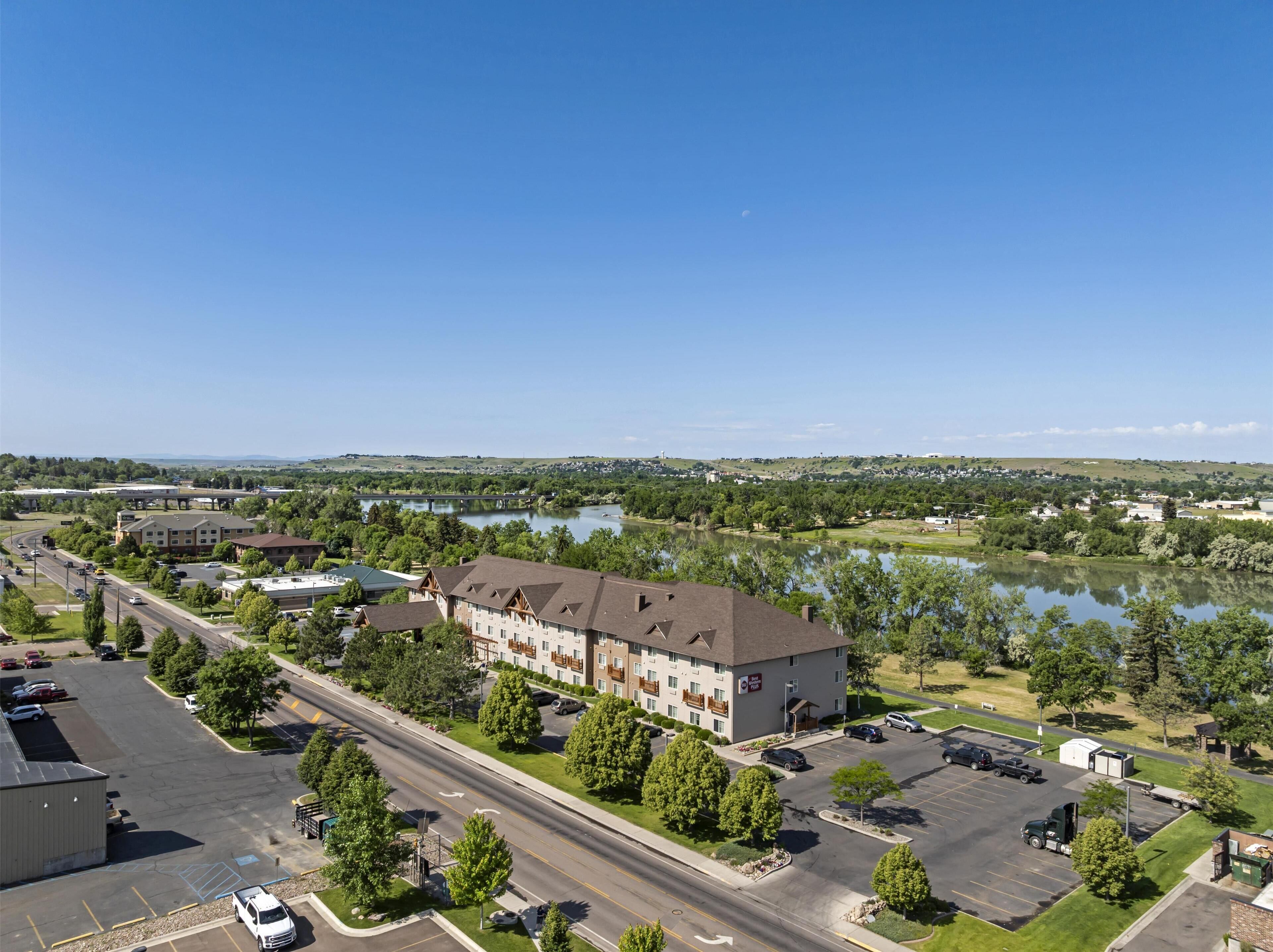 A hotel with a large parking lot, a river in the background, and a clear sky.