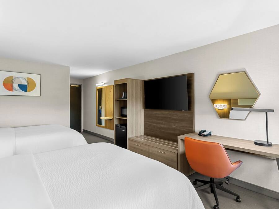 Quarto de hotel com duas camas, uma escrivaninha com cadeira, televisão e espelho.