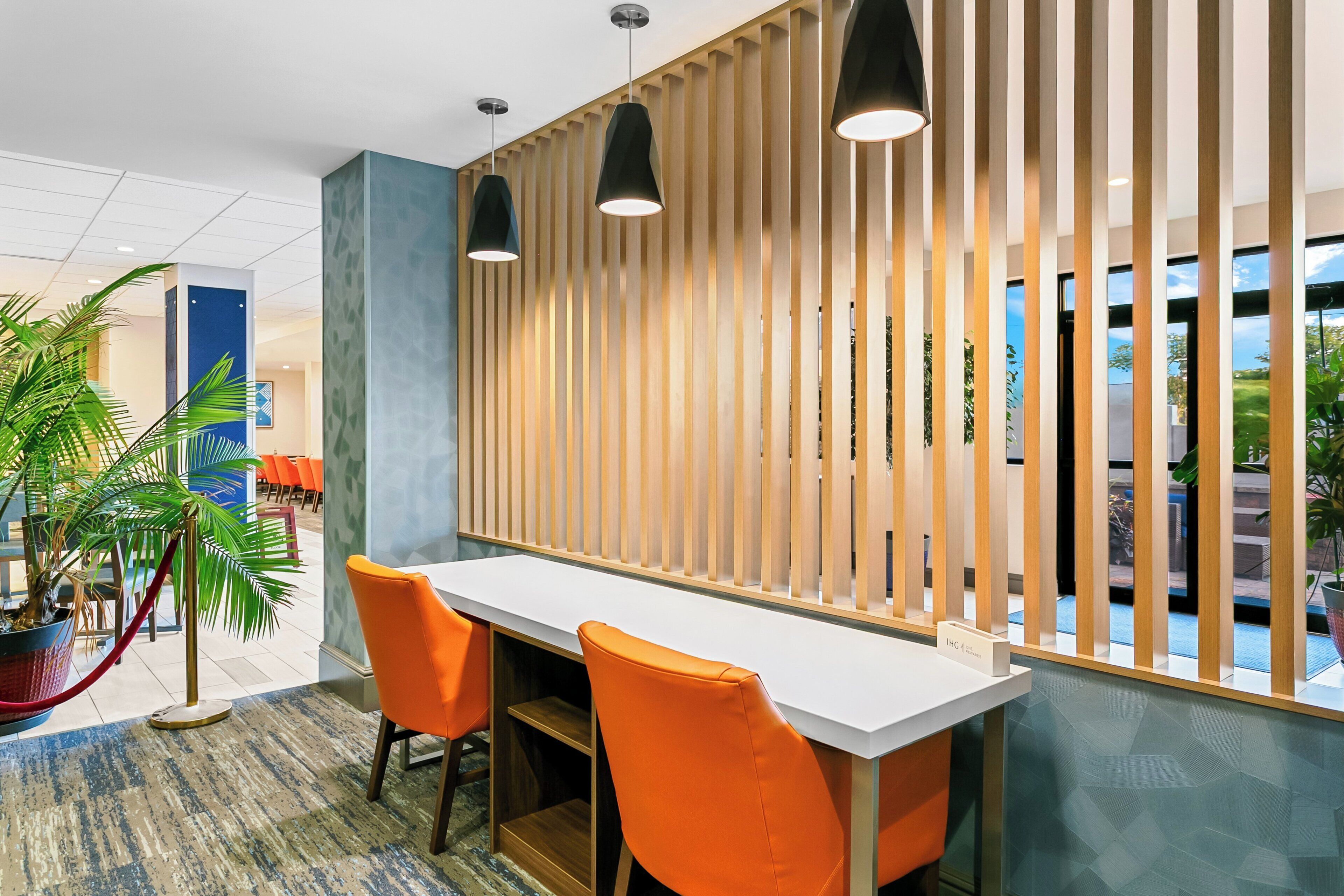 A modern interior with a long white table, two orange chairs, and a wooden slat partition.