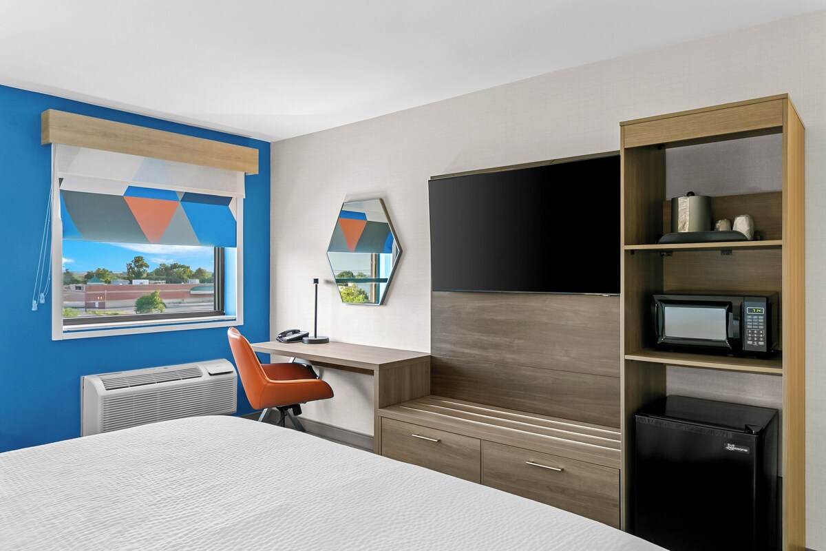 Habitación de hotel con cama, escritorio, silla, televisión de pantalla plana, microondas y refrigerador.
