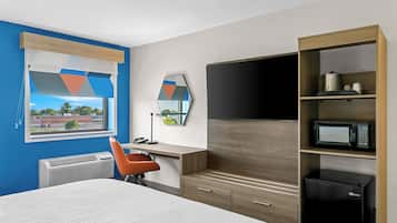 Habitación de hotel con cama, escritorio, silla, televisión de pantalla plana, microondas y refrigerador.