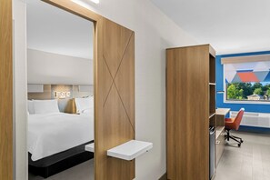 A modern hotel room with a bed, a desk, and a view of the outside.