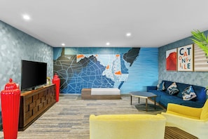 A modern living room with a large flat-screen TV, a red and white sofa, a yellow armchair, and a blue patterned wall. - Holiday Inn Express & Suites Baltimore West - Catonsville by IHG (Catonsville)