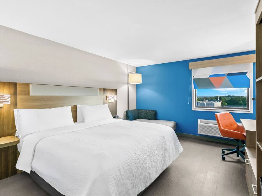 Habitación de hotel con cama, escritorio, silla, ventana con vistas y lámpara.