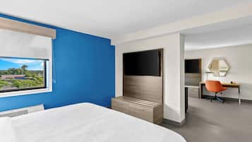 Quarto de hotel com cama, televisão, escrivaninha e cadeira, e janela com vista para o exterior.