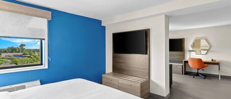 A hotel room with a bed, a television, a desk with a chair, and a window with a view of the outside.