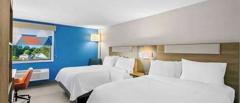 A hotel room with two beds, a desk, a chair, and a window with a view of houses.