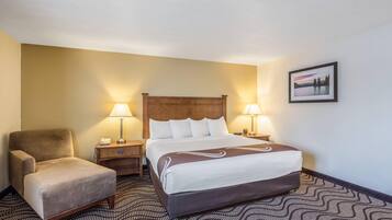 Une chambre d’hôtel avec un lit, deux lampes de chevet, une chaise, une table de chevet et un tableau encadré au mur.