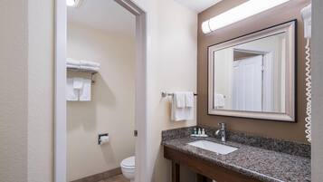 Un baño con lavamanos, espejo, toallero y retrete.
