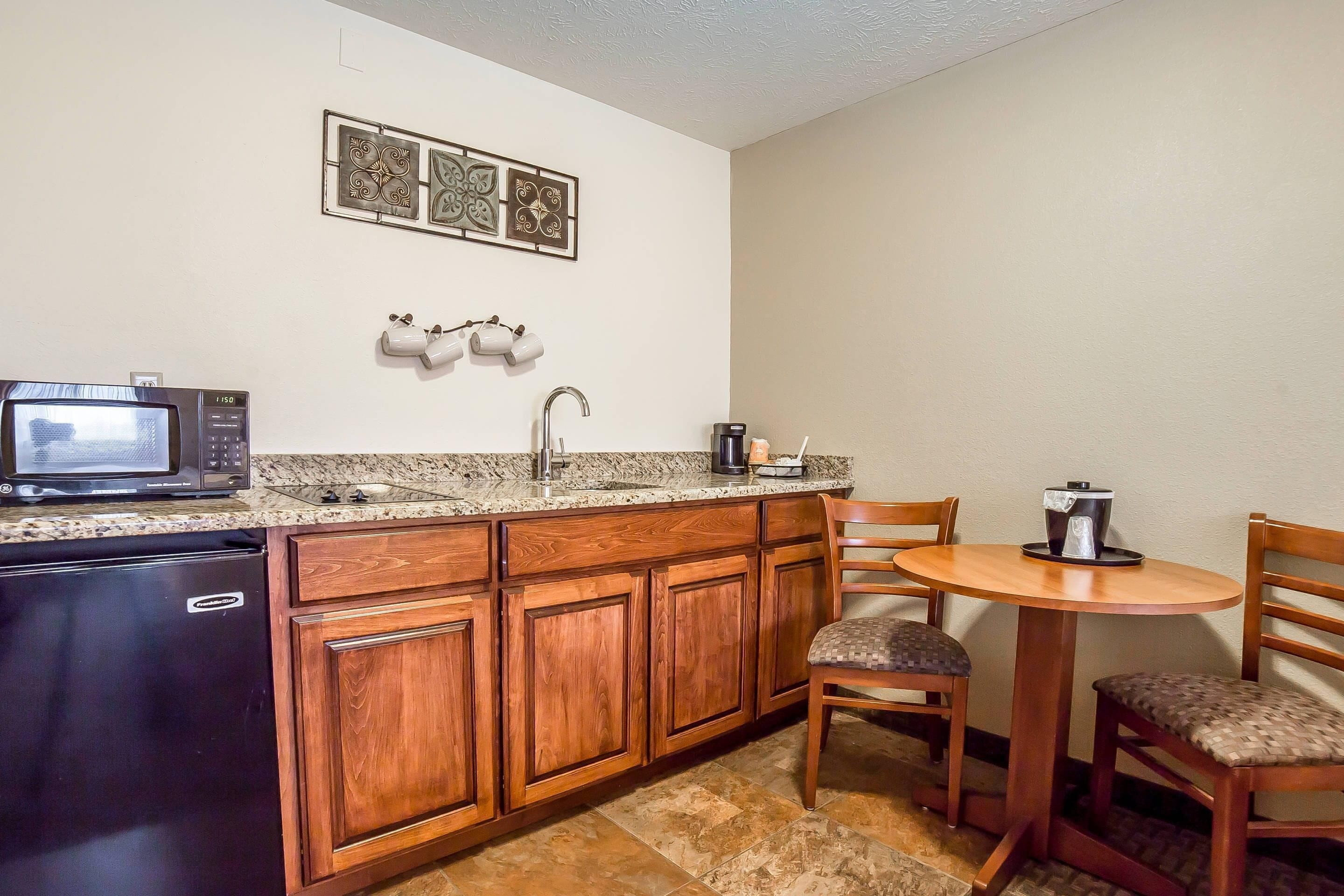 A compact kitchen with a microwave, sink, and coffee maker. There are wooden cabinets and a small dining table with chairs.