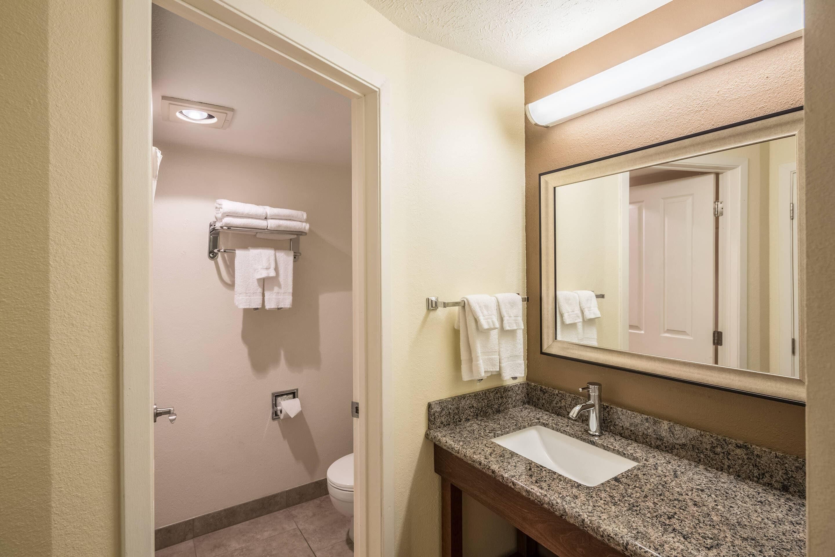 Un baño con lavamanos, espejo, toallero y retrete.