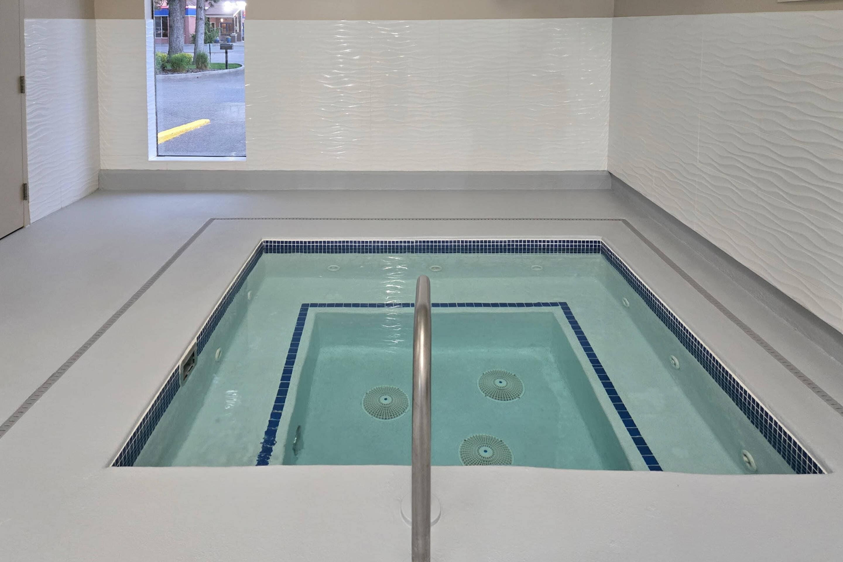 Piscina interior rectangular con agua azul cristalina, un desagüe central y vistas al exterior a través de una ventana.