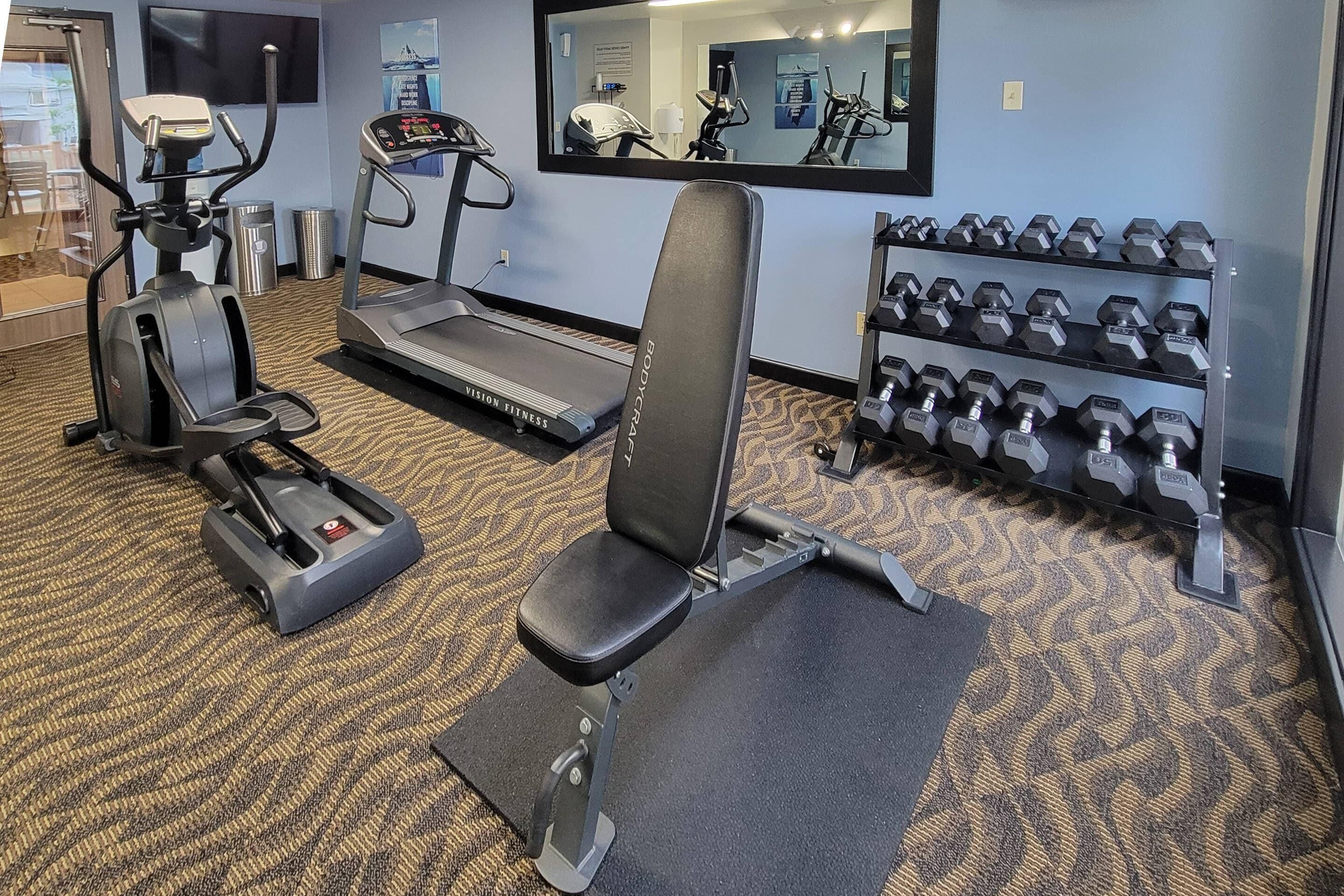 Un gimnasio con equipo de cardio, mancuernas y un espejo.